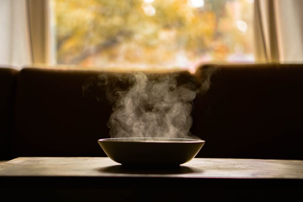 A steaming bowl of soup on a wooden table in soft daylight