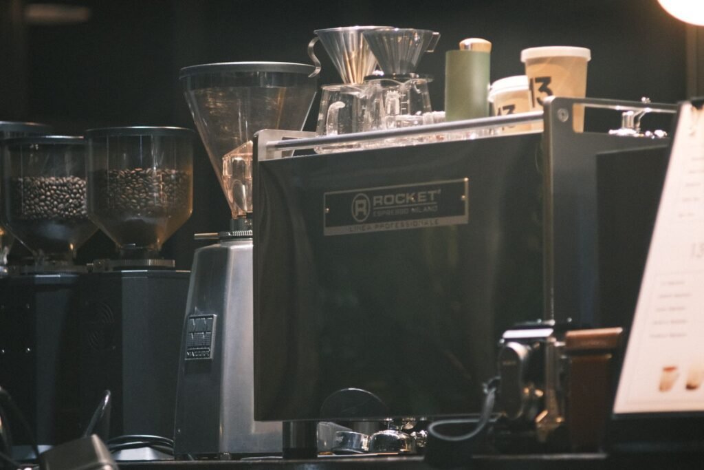 A chrome espresso machine on a cafe counter with grinders and stacked cups