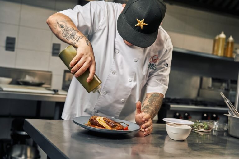A chef in a professional kitchen finishing a plated dish with sauce
