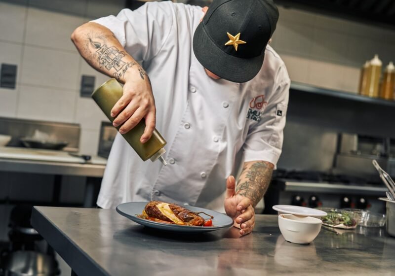 A chef in a professional kitchen finishing a plated dish with sauce