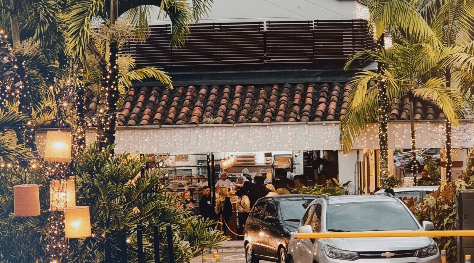 A Medellín street at dusk with palm trees and a lit restaurant entrance