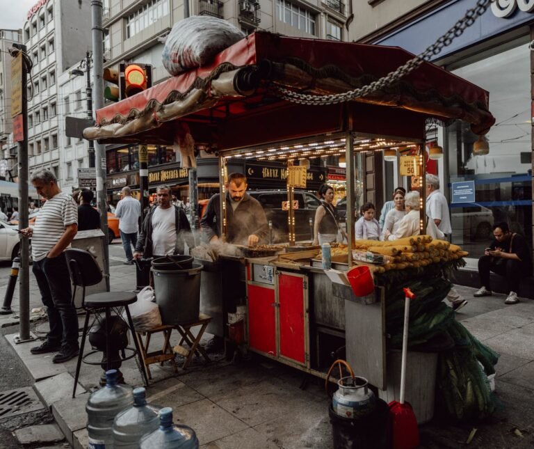 A street food vendor grilling at an outdoor cart with passers-by behind